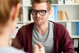 Junger Mann mit Brille im Gespräch mit seiner Therapeutin | © mediaphotos - Getty Images/iStockphoto